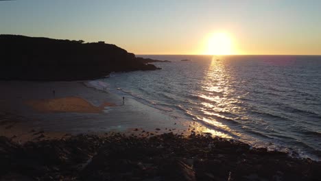 Aerial-shot-of-a-beautiful-sunset-surrounded-by-cliffs-in-Saussaye-beach,-Cancale,-France-and-the-Channel