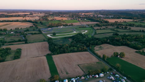 Linear-Tilt-Aerial-View-of-Camping-Lot-in-Rural-Area-with-Green-Field-and-Racing-Track-in-Background-at-Music-Festival