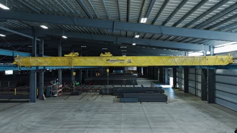 Aerial-panoramic-orbit-around-overhead-bridge-crane-in-steel-beam-warehouse