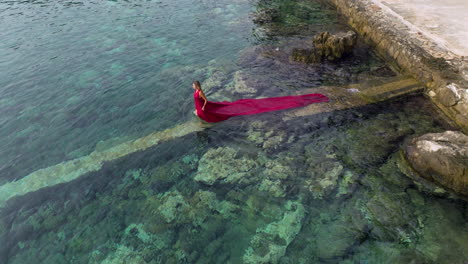 Mujer-Vestida-De-Rojo-Con-Un-Largo-Sendero-Nadando-En-El-Mar-Adriático-En-Croacia