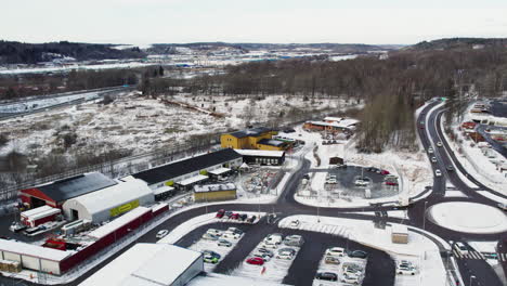 Stadsmissionens-second-hand-stores-in-snowy-gothenburg,-busy-road-nearby,-aerial-view