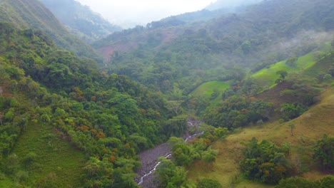 Aerial-drone-shot-following-a-dry-river-through-a-valley-between-mountains-surrounded-by-nature-in-Risaralda,-Colombia