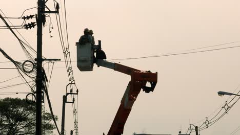 A-master-electrician-and-an-apprentice-are-on-a-crane-moving-closer-to-an-electrical-post-to-do-some-repairs-on-some-wire-connections