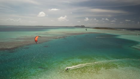 A-kitesurfer-gliding-over-clear-turquoise-waters-near-a-tropical-cay,-aerial-view