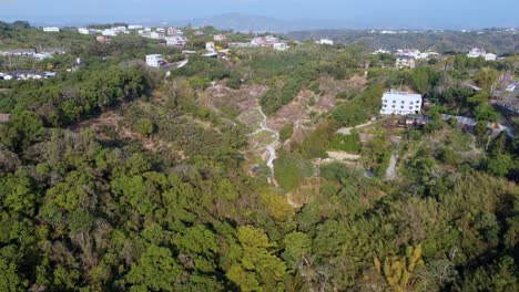 Lush-green-landscape-from-above-with-a-winding-path-and-scattered-houses-in-daylight,-aerial-view