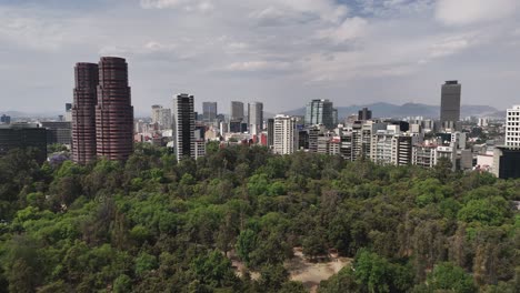 Drone-rising-above-Chapultepec-Park,-with-the-Polanco-neighborhood-in-CDMX-in-the-background