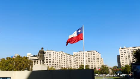 Cámara-Panorámica-Lenta-Chile-Bandera-Chilena-Ondeando-En-El-Viento-Sobre-El-Edificio-Del-Gobierno,-Arquitectura-De-La-Moneda,-Emblema-Nacional-En-El-Parque-Verde-Urbano-Y-El-Horizonte