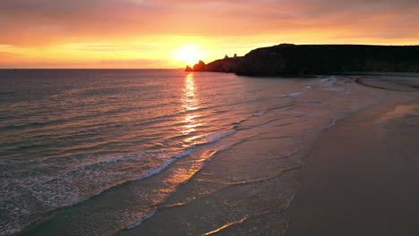 Lineare-Seitenluftaufnahme-Des-Sonnenuntergangs-über-Den-Wellen-Am-Leeren-Strand