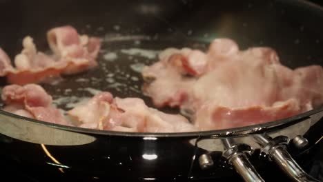 Closeup-skillet-of-defocused-bacon-frying,-sizzling-on-stove-top-pan