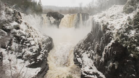 Winter-panorama-of-Pigeon-Falls-surging-from-snowmelt,-while-fresh-snow-falls-against-the-dramatic-backdrop