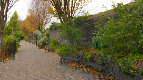Empty-Bench-On-A-Cobblestone-Pathway-In-Autumn-Park-In-Dublin,-Ireland