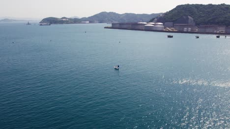 Aerial-drone-rotates-in-Japanese-Wakayama-beach-boats-mountain-range-environment-of-Japan,-Asia-in-summer,-blue-wide-ocean