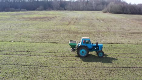Farmer-drive-old-tractor-and-spray-granular-fertilizer-on-green-wheat-field