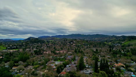 Aerial-view-of-a-residential-area-nestled-in-hilly-terrain-with-heavy-clouds-on-the-sky-and-horizon