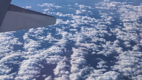 Wig-of-an-airplane-flying-above-dispersed-white-clouds-over-blue-skyline-closeup