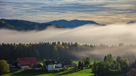 Mountain-forest-blanketed-by-clouds-at-dawn,-misty-dawn-atmosphere-outside,-sun-over-the-village