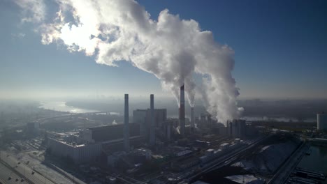 Aerial-wide-orbit-shot-of-a-coal-fired-heating-power-plant-with-thick-white-smoke-coming-from-the-chimneys-generating-gray-smog-over-the-horizon
