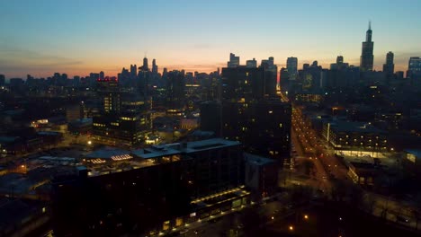 Eine-Faszinierende-Drohnen-Luftaufnahme-Von-Chicago-In-Der-Abenddämmerung,-Die-Beleuchtete-Wolkenkratzer-Vor-Dem-Dunkler-Werdenden-Himmel-Zeigt.-Die-Goldenen-Farbtöne-Der-Sonnenuntergangsfarbe-Heben-Architektonische-Wunder-Hervor.