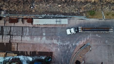 Drone-top-down-descend-on-semi-truck-and-trailer-loaded-with-steel-beams-driving-to-leave-factory