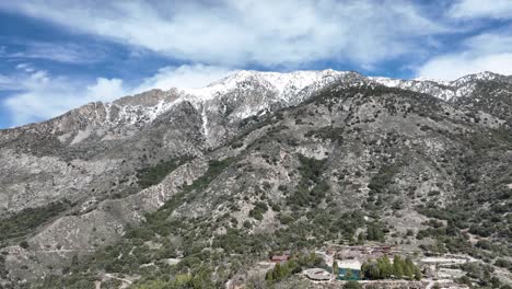 Casa-En-El-Bosque-Junto-Al-Arroyo-En-El-Bosque-Cae-En-El-Sur-De-California-Con-Montañas-Cubiertas-De-Nieve-En-El-Fondo-Transporte-Aéreo-En-Camiones-60fps