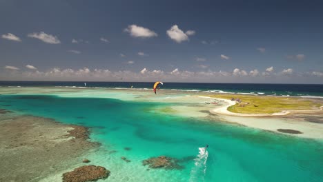 A-kitesurfer-gliding-over-clear-blue-waters-near-cayo-vapor,-los-roques,-venezuela,-aerial-view