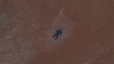 Birds-eye-view-of-man-lying-on-wide-expanse-of-cracked-desert-ground