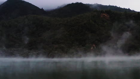 Zoom-out-shot-of-steam-rising-over-geothermal-pond-in-volcanic-region,-New-Zealand,-North-Island