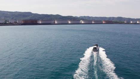 Luftdrohne-Folgt-Motorboot-Von-Unten,-Das-Blaue-Japanische-Meer-Segelt,-Küste-Mit-Gebirgskette-Im-Hintergrund,-Japanisches-Reiseziel-Wakayama
