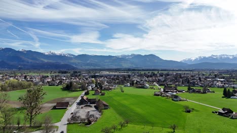 Drone-flight-over-green-rural-fields-and-swiss-town-in-sunlight