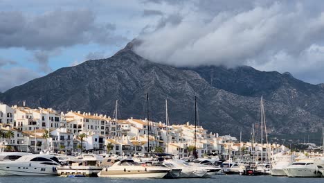 Primer-Plano-De-Una-Montaña-Alta-En-Puerto-Banús-Rodeada-De-Casas-Blancas-Y-Barcos-Anclados-En-El-Puerto,-España