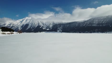 Areal-shoot-of-a-frozen-lake,-surrounded-by-mountains-on-a-beautiful-sunny-day