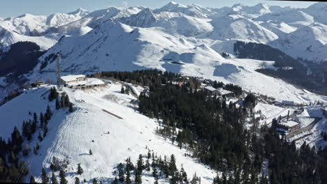 A-snowy-mountain-resort-with-ski-slopes,-lifts,-and-alpine-trees,-under-a-clear-blue-sky,-aerial-view