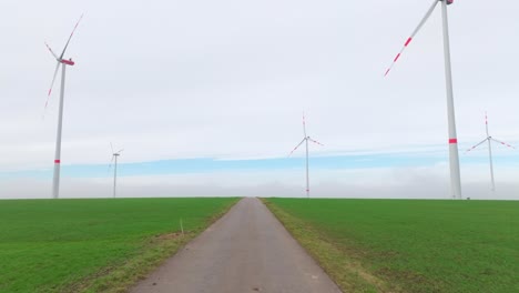 Straße-Durch-Den-Windpark-Mit-Windrädern-über-Der-Grünen-Wiese