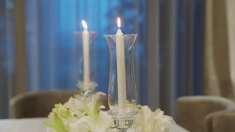 Velas-Blancas-Encendidas-En-Candelabros-De-Cristal-Altos-En-La-Mesa-Del-Comedor