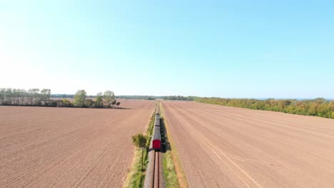 Aerial:-steam-narrow-gauge-railway-in-the-countryside-passing-by-sown-fields,-Flying-above-the-train