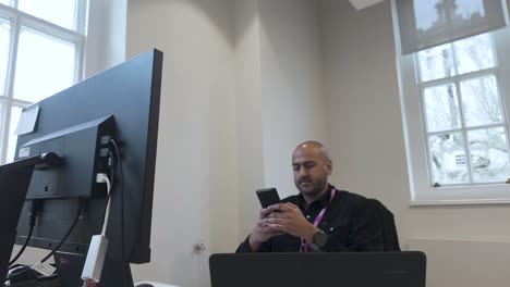 Man-Using-Mobile-Phone-In-Front-Of-His-Computer-In-The-Office