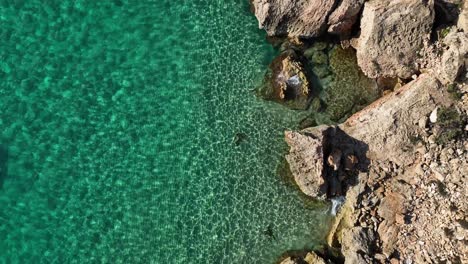 Glitzerndes-Kristallklares-Meer-Mit-Felsigem-Strand,-Draufsicht,-Drohnenaufnahme