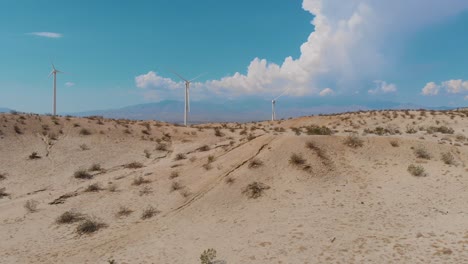 Slow-side-scroll-of-sand-and-rush-covered-hills-near-small-desert-town-and-green-energy-wind-farm