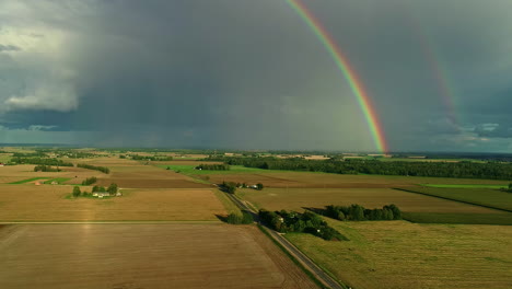 Beautiful-shot-of-two-rainbows-on-the-horizon,-surrounded-by-a-field,-a-road-and-nature