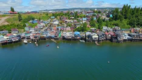 Panoramic-aerial-view-establishing-over-the-stilt-houses-of-Castro-in-Chiloe,-parallax-effect,-sunny-day,-high-tide