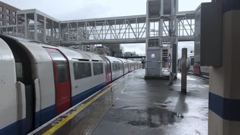 PIccadilly-Line-Train-Arriving-At-Acton-Town-Station-Platform-On-Wet-Overcast-Day