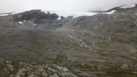 Ein-Großer-Gletscher-Auf-Einem-Felsigen-Berg-Mit-Einigen-Kleinen-Wasserfällen-Und-Flüssen-In-Einer-Nebligen-Umgebung,-Norwegen,-Europa,-Drohne