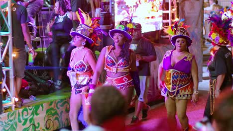 Un-Grupo-De-Mujeres-Bailan-Sonriendo-Y-Saludando-A-La-Cámara-Mientras-Se-Pavonean-En-El-Desfile-De-Carnaval-Por-La-Noche.