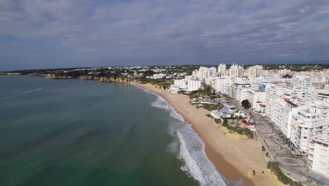 Aerial-establishing-shot-of-Waterfront-Armação-de-Pera-buildings,-Sandy-beach-and-promenade,-Algarve