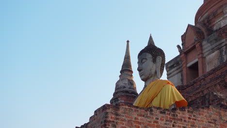 Large-Buddha-statue-with-orange-robe-at-Ayutthaya-Historical-Park,-Thailand,-against-blue-sky