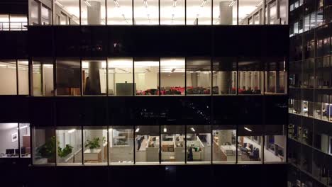 Man-using-vacuum-cleaner-tidying-corporate-workspace-in-skyscraper-office-at-night