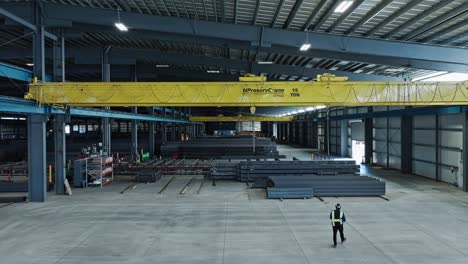 Worker-in-safety-vest-operates-overhead-bridge-crane-in-steel-warehouse