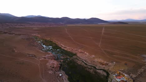 A-meandering-stream-in-the-vast,-arid-landscape-of-chile-at-dusk,-aerial-view