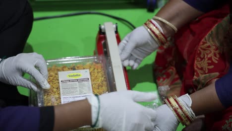 Cinematic-Shot-men-are-sealing-the-boxes-of-savory-food-and-inside-the-seal-machine-and-arranging-them-inside-the-big-books