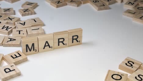 Closeup-hand-places-Scrabble-tiles-on-edge-to-form-word-MARRIAGE